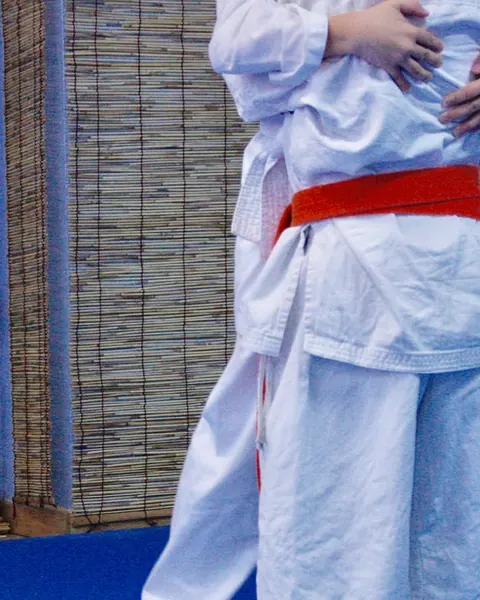 Un karateka amb el quimono blanc i el cinturó vermell, al costat de la paret de canyes del dojo