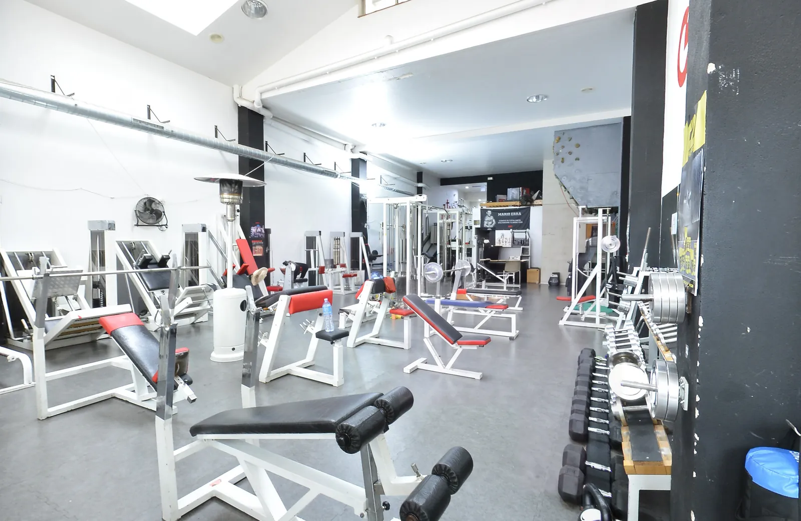 La sala de musculació del CEEC: màquines blanques amb tapisseria vermella, pilars negres i, al fons, la pancarta de campió de Mario Erra