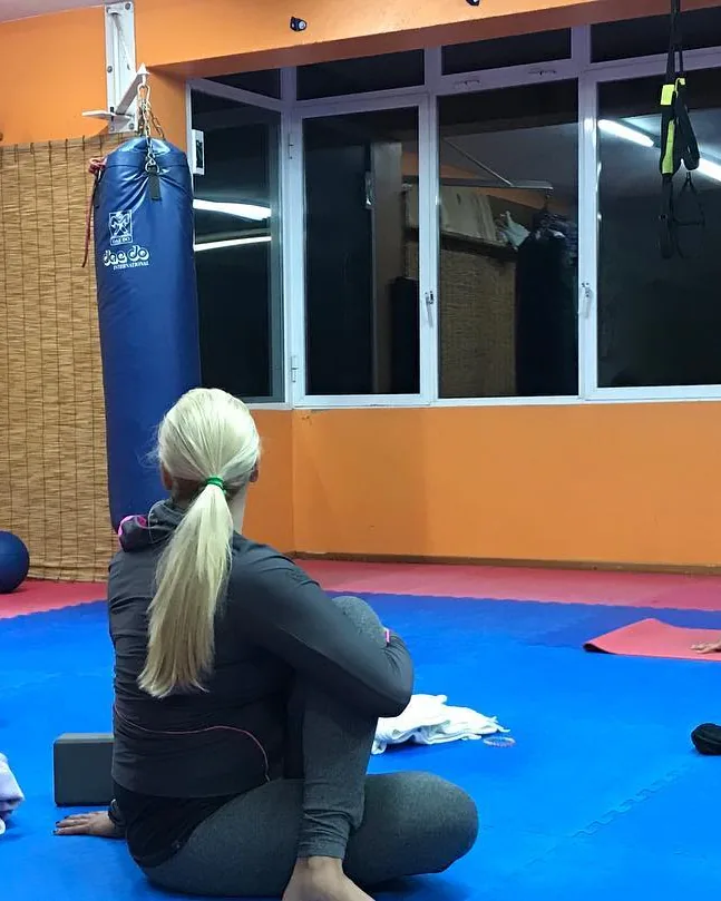 Una noia d'esquena, asseguda al tatami del dojo en una classe d'estiraments